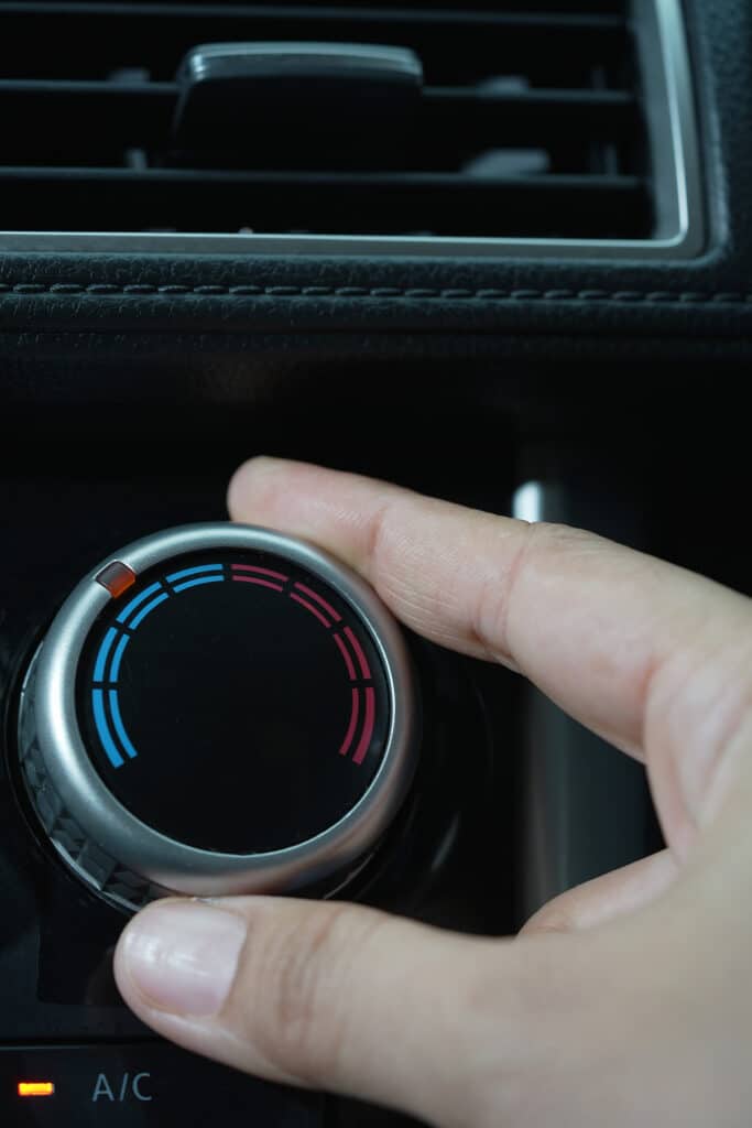 Main ajustant le bouton de température (bleu/froid à rouge/chaud) d'une voiture, A/C allumé.