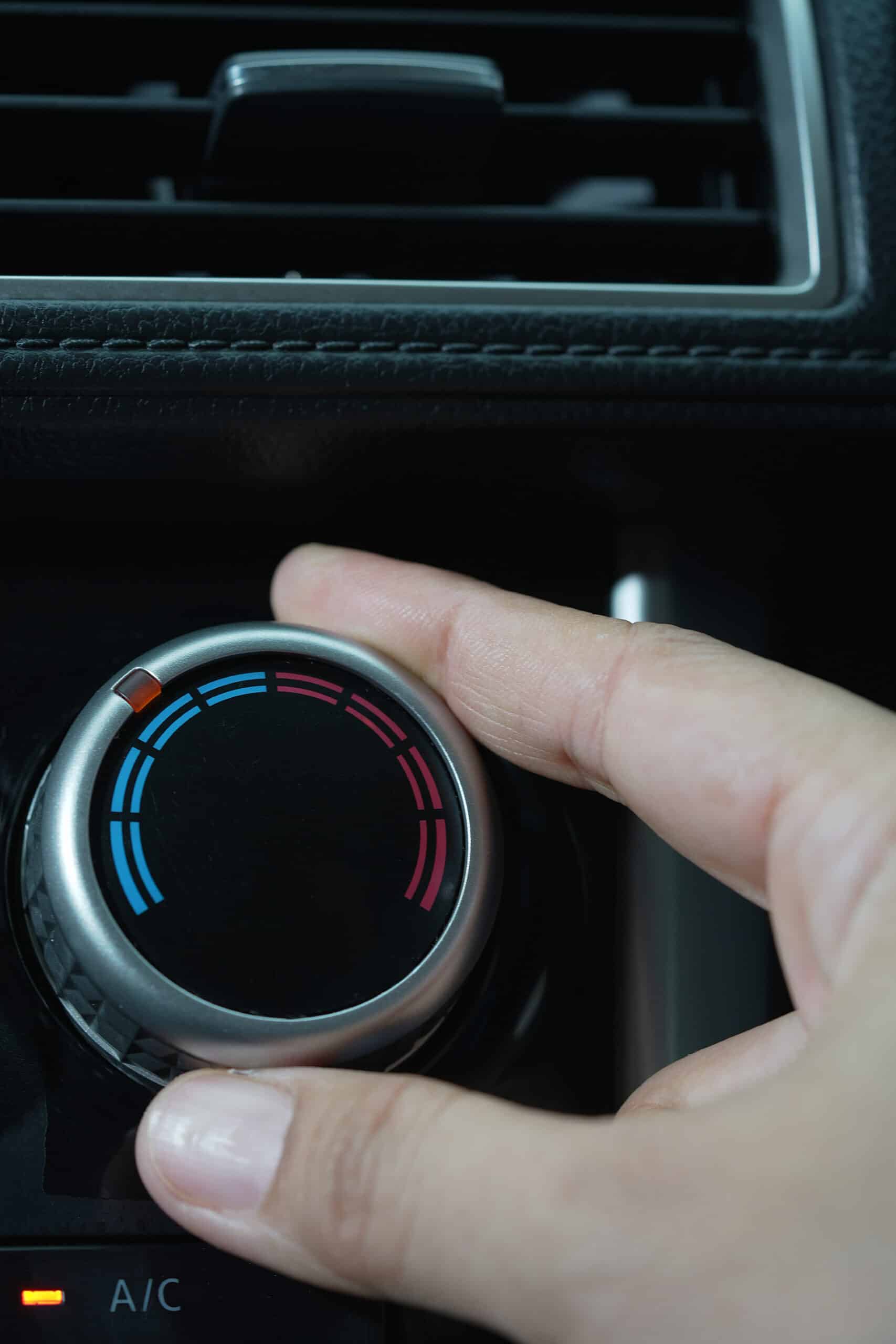 Main ajustant le bouton de température (bleu/froid à rouge/chaud) d'une voiture, A/C allumé.