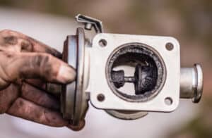 Mécanicien tenant une vanne EGR diesel fortement encrassée de suie noire, nécessitant nettoyage ou remplacement.