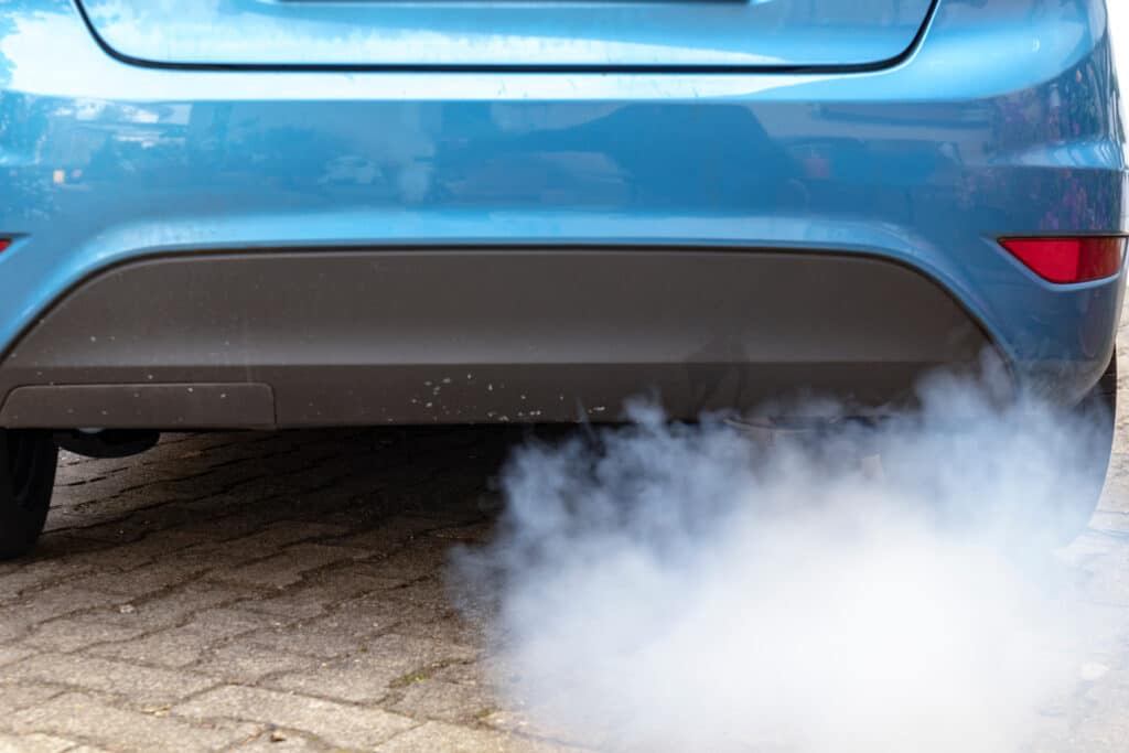 Voiture bleue émettant fumée blanche échappement Gros plan sur l'arrière d'une voiture bleue dégageant une épaisse fumée blanche par l'échappement sur un pavé.